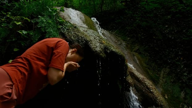 Young woman drinking water from cascade waterfall at deep tropical rain forest. Creative. Female hiker drinking water from mountainous spring