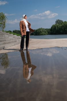 A young woman wearing a hijab stands next to a large puddle