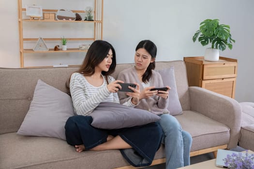 Asian lesbian couple gaming together on the sofa at home. Concept of love, bonding, and leisure activities in a cozy indoor setting.