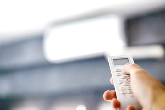 Man's hand holding air conditioning unit remote control. Man operating air conditioner with remote control indoors.