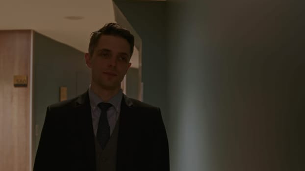Security man walking along rooms in hotel corridor. Stock clip. Young man in suit in a dark building hall
