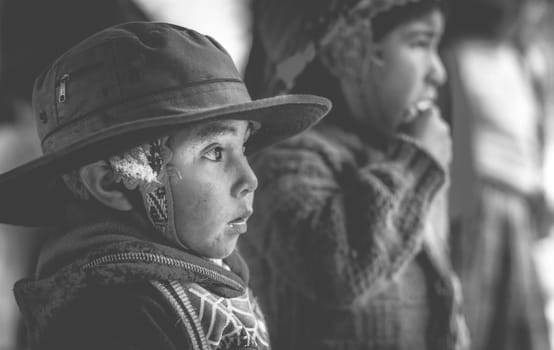 Peru, Cusco - 13 October 2018: Little boy in big brown titfer attentively looking, in Cusco. Black and white photo.