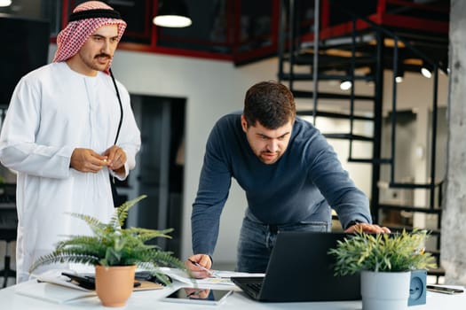 Arab and European business men working together in a modern office with laptop