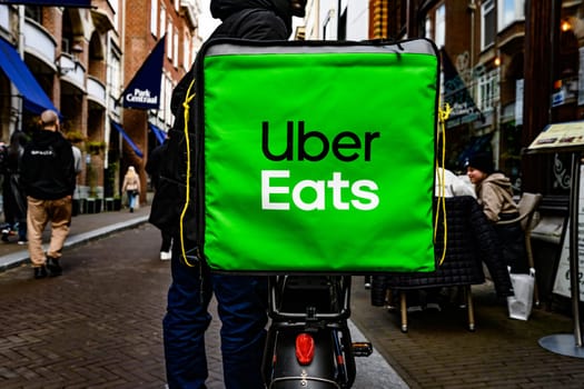 Hague, Netherland - 09 April 2023: Big green Uber Eats Food Bag. Food delivery man by bicycle