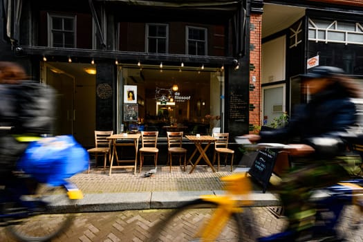 Hague, Netherland - 09 April 2023: Blurry bikers on a street of Hague. Cozy Cafe in the center of a touristic place in Holland.
