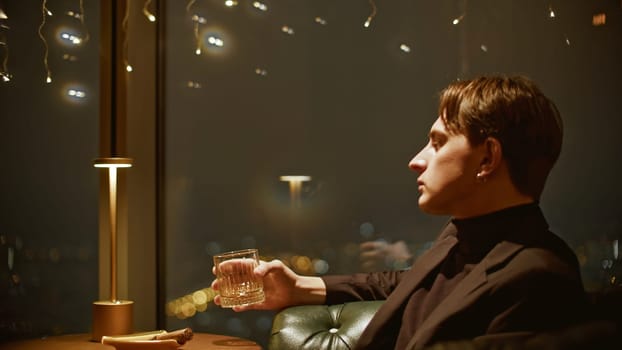 Young attractive man drinks whiskey in restaurant. Media. Young single man in suit drinks scotch in restaurant. Cinematic handsome man in suit at whiskey restaurant.