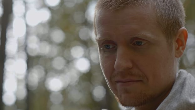 Close-up of man smiling and talking in woods. Stock. Cinematic portrait of man in style of teacher in forest. Man speaks and smiles like sensei.