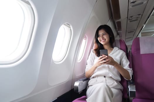 Asian businesswoman using smartphone on airplane during flight.