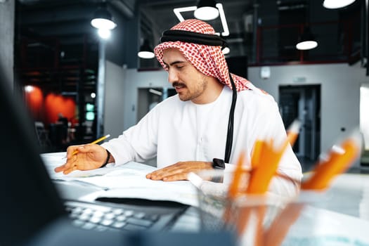 Young muslim businessman in traditional outfit working at the table in office clsoe up