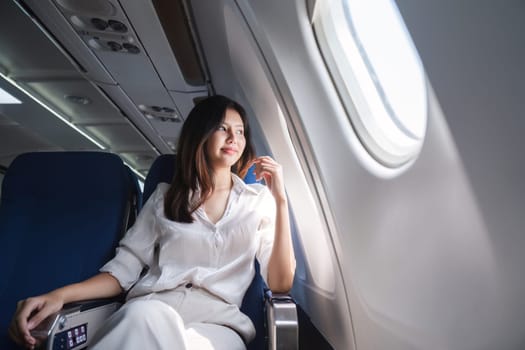 Asian woman looking out airplane window during flight.
