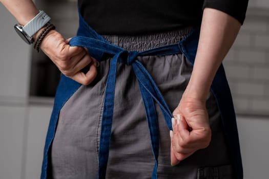 Female Hands Are Tying A Kitchen Apron Behind In Close-Up View