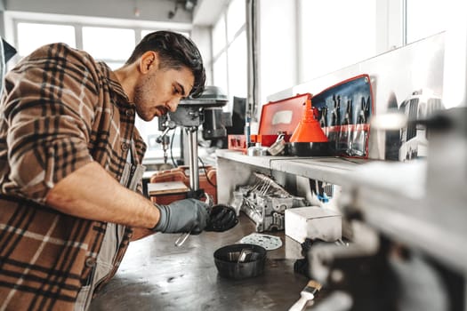 Young man mechanic repairing car parts on worktable in car service shop close up