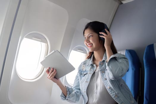 Asian woman using tablet and headphones on airplane during flight.