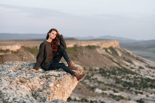 Serene sunset woman perched on cliff gazing at valley and mountains in the distance