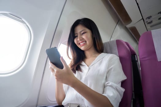 Asian businesswoman using smartphone on airplane seat during flight.