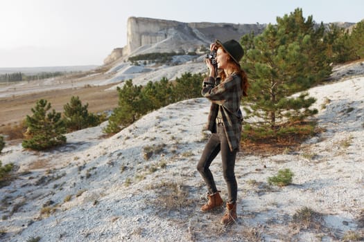 Woman in hat and plaid shirt standing on hill overlooking majestic mountain landscape