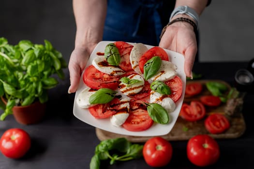 Woman Holds Caprese Salad On Plate, Close-Up Of Tomatoes And Mozzarella Cheese