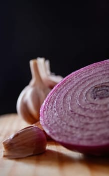 Purple onion and garlic on brown board. Dark background