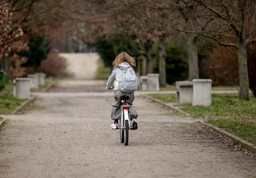 Girl Rides Bicycle Through Spring Park, View From Behind