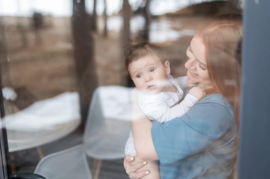 View through the window of a red-haired Caucasian woman holding her little son