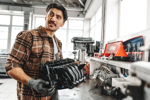 Young man mechanic repairing car parts on worktable in car service shop close up