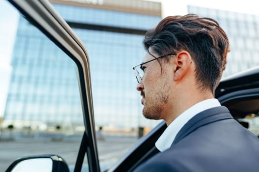 Young handsome businessman in a suit comes out of the luxury car close up