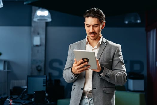 Young successful businessman working on digital tablet while standing in office close up