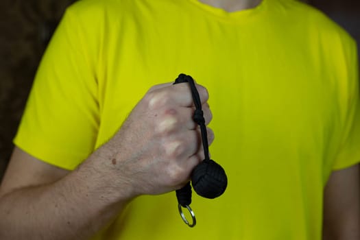 Self-defense keychain made of braided laces with monkey knot with metal ball, baton for self-defense against a criminal on man hand