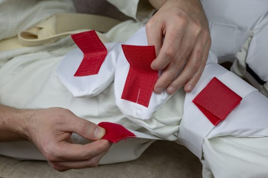 Kyokushin karate athlete puts on protective equipment on his knees, Velcro fixing shin guards on legs for martial arts