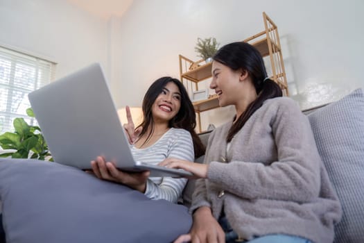 Asian lesbian couple using laptop together at home. Concept of technology and companionship.