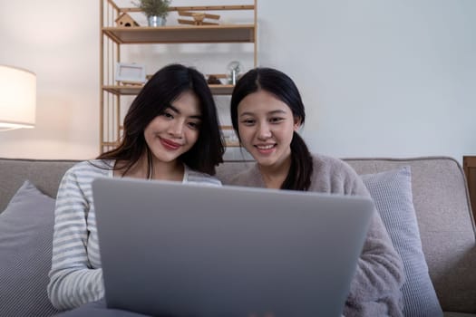 Asian lesbian couple using laptop together at home. Concept of technology and companionship.