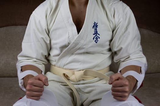 Kyokushinkai karate athlete with white belt and special protective equipment and kimano sits before the competition
