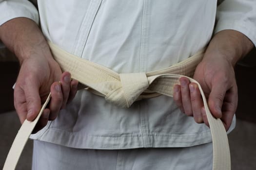 Karate athlete ties white belt on kimono, the equipment of an Asian martial arts fighter