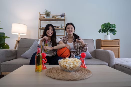 Asian friends cheering while watching basketball at home. Concept of sports and friendship.