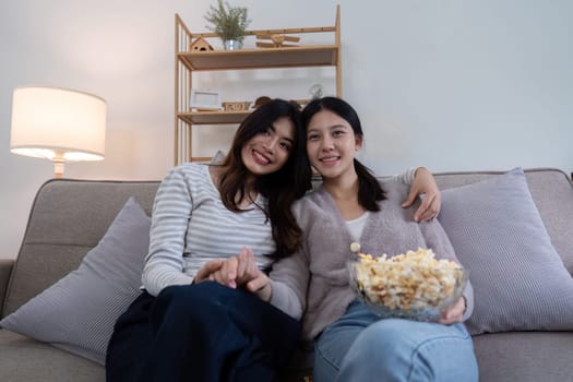 Asian lesbian couple relaxing at home with popcorn. Concept of friendship and leisure.