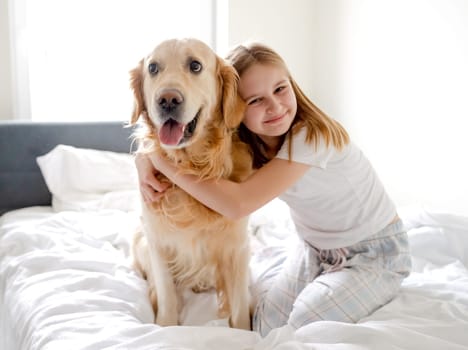 Girl Poses With Golden Retriever In Bed In The Morning In A Bright Room