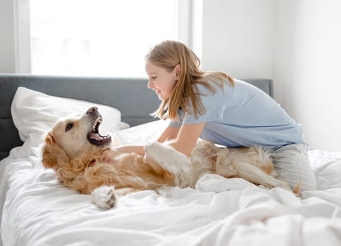 Girl Plays With Golden Retriever In Bed In The Morning In A Bright Room