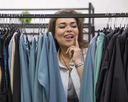 Portrait of a fat woman in a plus size store through hangers with clothes