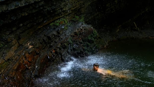 Child boy swimming in mountain pond with waterfall. Creative. Child on summertime vacation refreshing in river