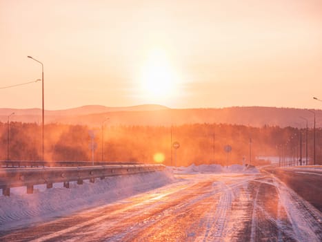 The sun rises beautifully over a snow-covered road in a serene winter countryside.