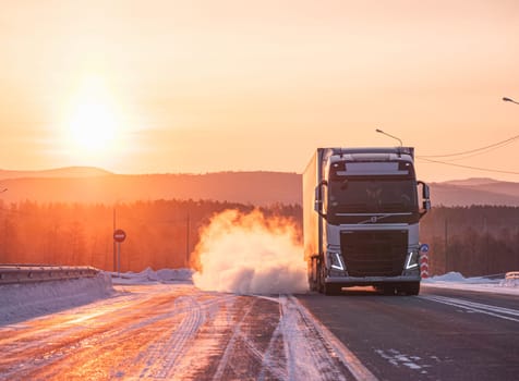 Large truck driving along a snow-covered highway during a breathtaking winter sunrise.