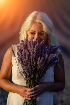 Blonde woman poses in lavender field at sunset. Happy woman in white dress holds lavender bouquet. Aromatherapy concept, lavender oil, photo session in lavender.