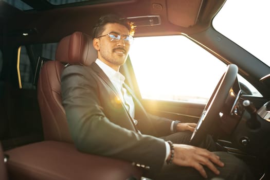 Young businessman in elegant suit driving luxury car close up