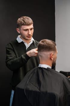 Young barber carefully cuts the mans hair with a trimmer in the bustling barbershop
