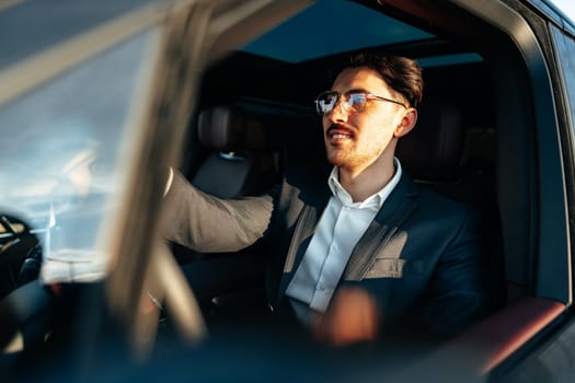 Young businessman in elegant suit driving luxury car close up