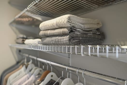 A closet with clothes hanging on hangers and a basket of clothes on the top shelf. The clothes are neatly folded and organized