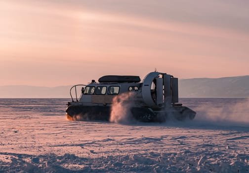 Hovercraft driving at high speed on snow covered frozen ice surface of Lake Baikal at dusk.