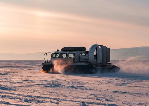 Hovercraft driving at high speed on snow covered frozen ice surface of Lake Baikal at dusk.