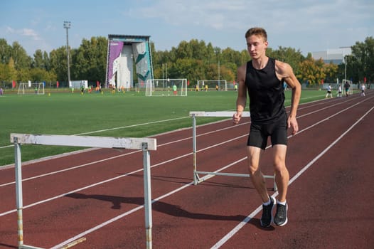 Young sporty man athlete runner in sportswear stretching before running hurdles on stadium