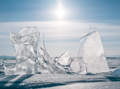 The serene landscape of Lake Baikal in winter, featuring captivating, transparent ice formations under a bright sky with the sun shining brightly above.